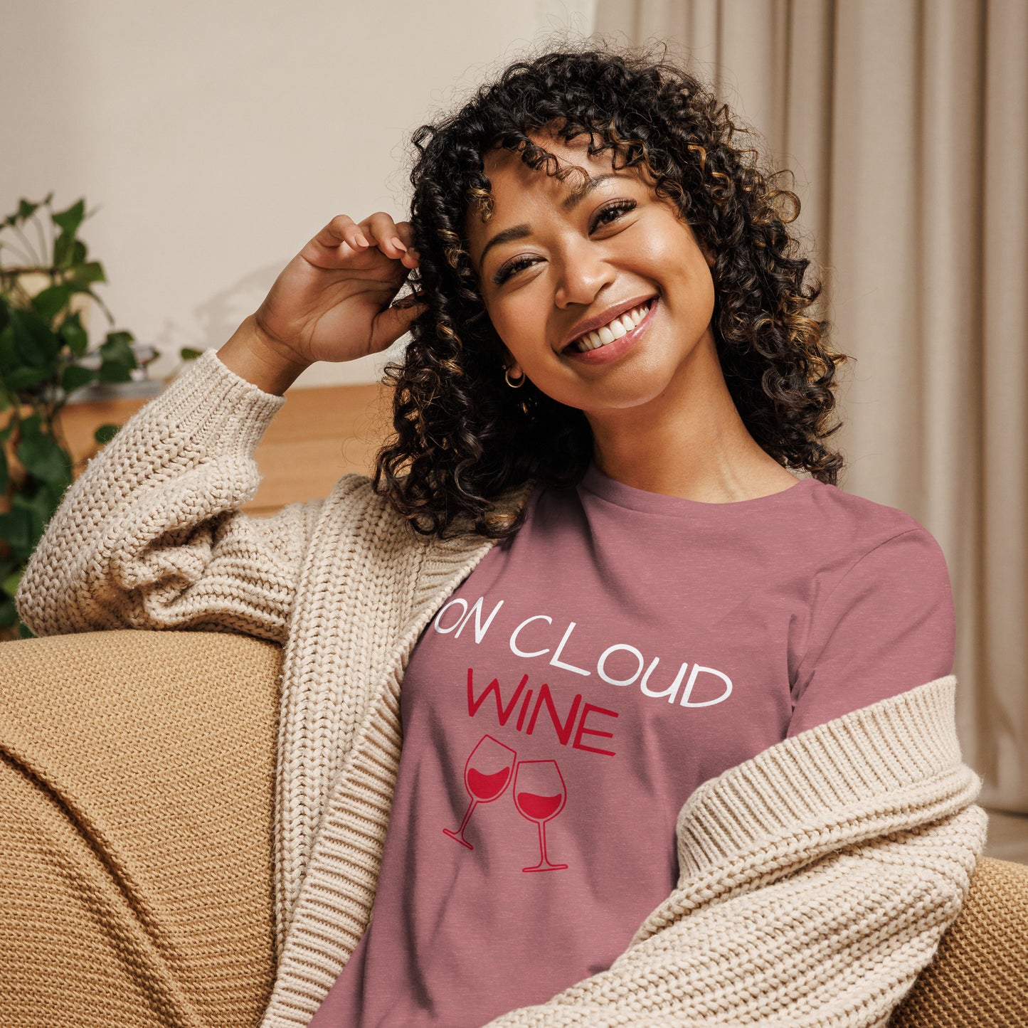 Woman wearing "On Cloud Wine" ladies T-shirt, smiling while lounging comfortably in a cozy room.